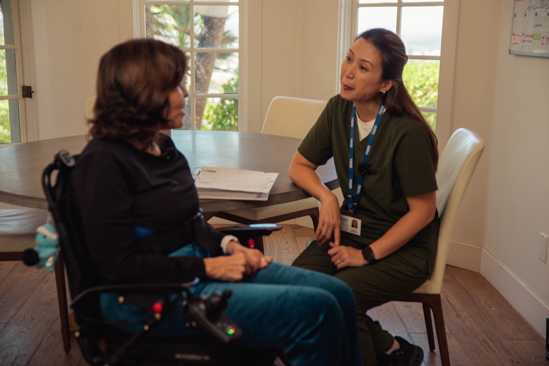A caregiver and client talking together at a sunlit dining table