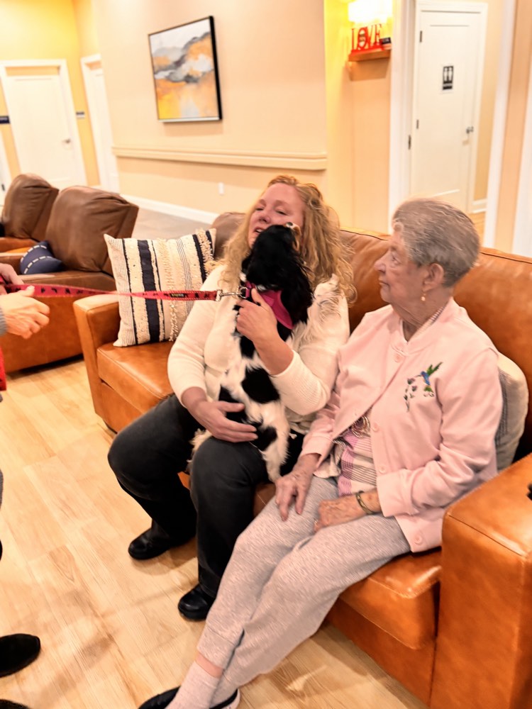 A caregiver and her client enjoying a visit from a dog