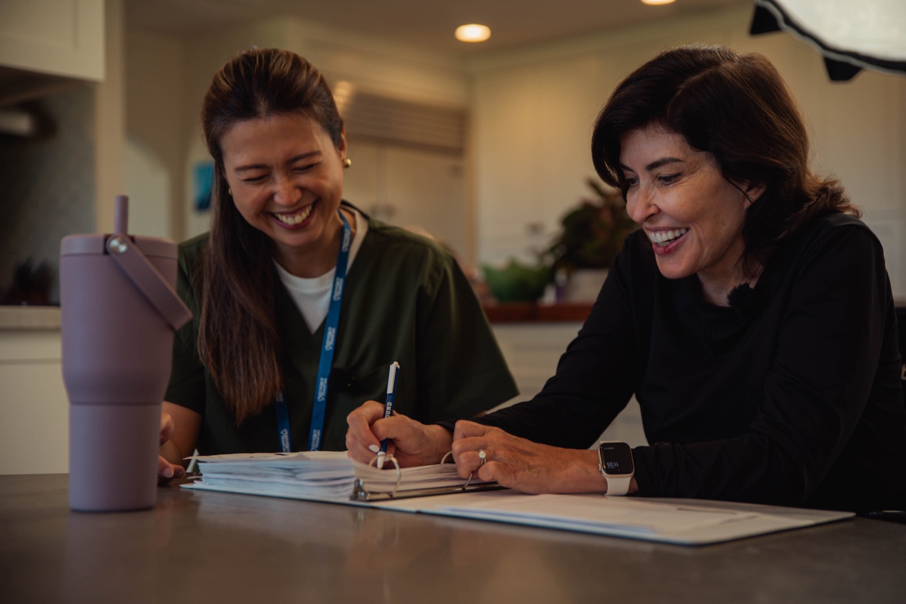 A caregiver and client laughing together while reviewing a daily care planner